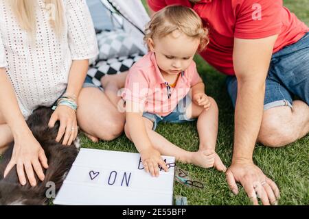 Porträt eines Kleinkindes und seiner Eltern, die eine Ankündigung über ein neues Baby machen. Kind Spaß mit seinen Eltern und spielen auf dem Rasen mit lett Stockfoto