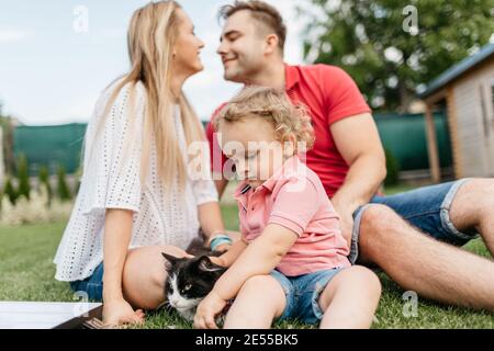 Glückliche Familie verbringen Zeit zusammen draußen im Garten. Kind Spaß mit seinen Eltern und spielen auf dem Rasen mit einer Katze. Stockfoto