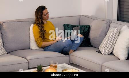 Junge Frau sitzt mit ihrem Laptop auf der Couch Stockfoto