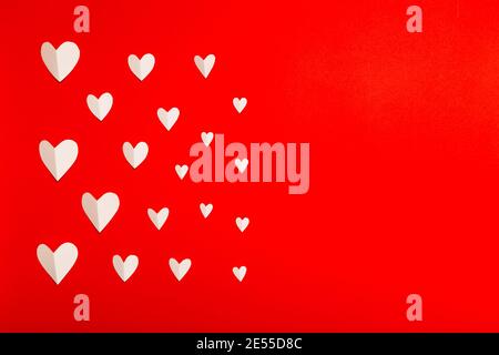 Komposition zum Valentinstag. Weiße Papierherzen auf rotem Hintergrund im flachen Lay-Stil. Valentinstag Konzept, Foto Vorlage Stockfoto