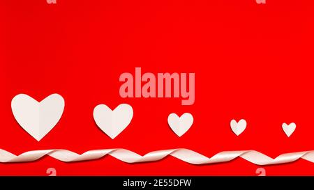 Banner. Weiße Papierherzen mit weißem Farbband über dem roten Hintergrund in flacher Lay-Optik. Komposition zum Valentinstag. Urlaubskonzept. Stockfoto