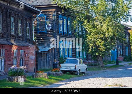 Gepflasterte Straße mit klassischen sowjetischen Moskwitsch 408 Auto und traditionellen sibirischen Holzhäusern in Tomsk Oblast, Sibirien, Russland Stockfoto