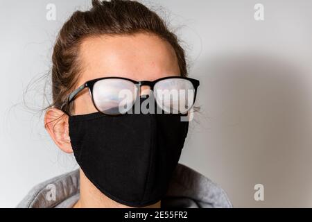 Junger Mann mit nebliger Brille, verursacht durch das Tragen einer Schutzmaske. Schutzmaßnahme während einer Coronavirus-Pandemie Stockfoto