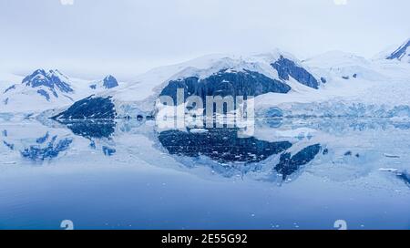 Reflexionen von Bergen und dem schneebedeckten und blauen Eis Ein Gletscher im ruhigen Wasser der Antarktis in der Abenddämmerung Stockfoto