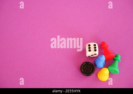 Verschiedene farbige Brettspiel-Figuren und Würfel in der rechten Ecke der lila rosa Tapete Hintergrund Stockfoto