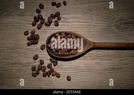 Kaffeebohnen in einem alten Holzlöffel auf einer strukturierten Oberfläche aus Holz. Stockfoto