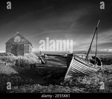 Der zerfallende Rumpf eines Klinker gebauten Bootes liegt auf Thornham Sumpf neben der Kohle Scheune. Stockfoto