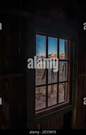 Majestätischer Blick auf rote Felsenmesas durch das Fenster eines alten Pionierhauses. Die Aussicht ist die gleiche, aber die Leute sind weg. Stockfoto