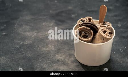 Gerolltes Eis mit in-Cone-Tasse auf dunklem rustikalem Hintergrund. Iced Rolls mit Keksen Schokolade Sandwich Cookies. Thai-Stil gerolltes Eis mit Platz für Text oder Design. Banner. Stockfoto