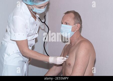 Der Arzt lauscht mit einem Stethoskop auf die Lungen alter Männer. Gesundheitscheck vor der Coronavirus-Impfung. Stockfoto