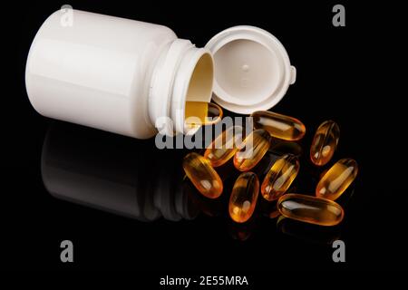 Omega-3 Kapseln auf schwarzem Hintergrund. Gesundheitskonzept mit Fischölkapseln. Weiße Flasche Stockfoto