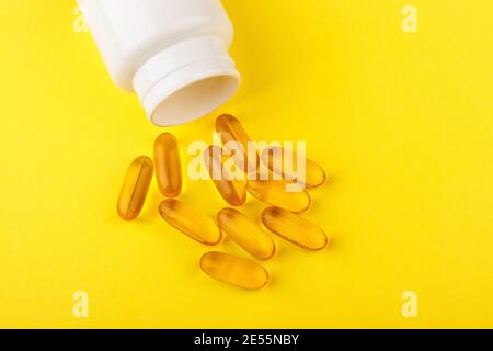 Gelbe Vitamin D Pillen auf gelbem Hintergrund und weißem Plastikglas. Medizin Gel Tabletten von Vitamin d auf dem Tisch. Gelbe Vitamin D-Ölkapsel hält Stockfoto