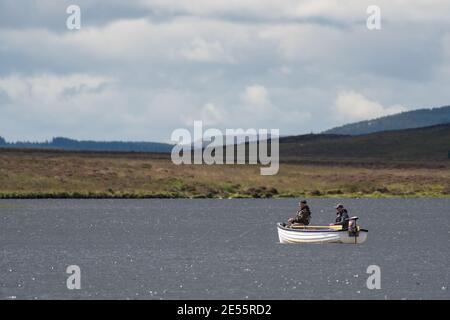 Zwei Männer (70s) Fliegenfischen auf Forellen in einem weißen Boot Auf einem schottischen Moorland loch oder See Stockfoto