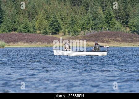 Zwei Männer (70s) Fliegenfischen auf Forellen in einem weißen Boot Auf einem schottischen Moorland loch oder See Stockfoto