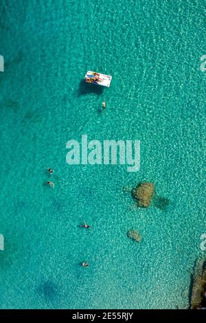 Eine Luftaufnahme eines Strandes in Griechenland mit Teenagern, die auf einem Wasserfahrrad paddeln. Stockfoto