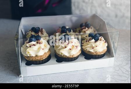 Ein Mädchen Koch in einer grauen Schürze verpackt Cupcakes mit Sahne in einer Geschenkbox, um die Bestellung an den Kunden zu senden. Stockfoto