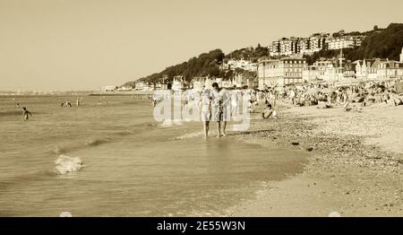 Die Leute entspannen sich am Strand. Trouville-sur-Mer und das nahe gelegene Deauville sind beliebte Sommerresorts in der Normandie. Paar laufen. Sepia historisches Foto Stockfoto