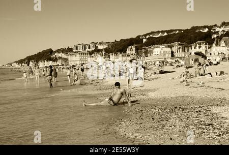 Junger Mann, der am Strand mit Shisha relaxt. Trouville-sur-Mer und das nahe gelegene Deauville sind beliebte Sommerresorts in der Normandie. Sepia historisches Foto Stockfoto