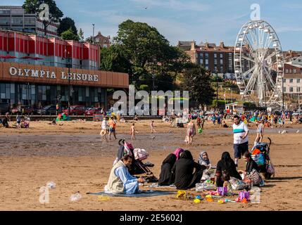 Eine Familie am Strand von Scarborough mit den Frauen, die Kopftücher und ein Riesenrad im Hintergrund tragen. Stockfoto