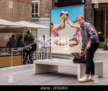 Junger Mann, der beim Retro-Poster steht und verwirrt in der Nähe von Kings Cross aussieht. Stockfoto