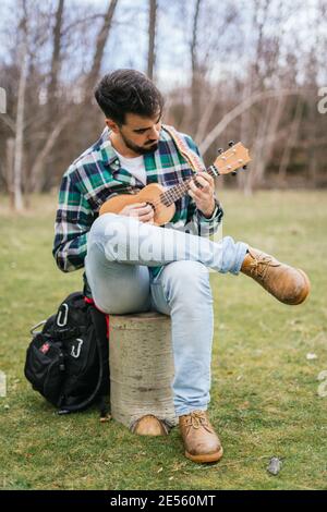 Vertikale Nahaufnahme eines hispanischen Mannes, der ein Lied spielt Seine Ukulele im Wald Stockfoto