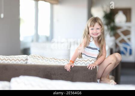 Kleines lächelndes Mädchen sitzt mit ihren Beinen auf der Couch Stockfoto