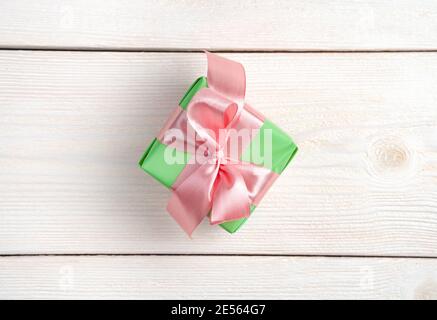 Eine kleine hellgrüne Geschenkbox mit einem rosa Band auf einem weißen Holzhintergrund. Stockfoto