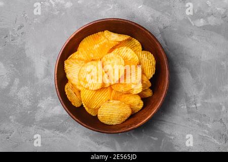 Gebratene gewellte goldene Kartoffelchips in brauner Holzschüssel auf Betonhintergrund, Draufsicht Stockfoto