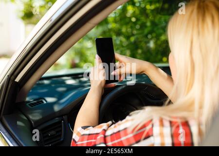 Junge Frau schaut in einem Auto auf ihr Smartphone.