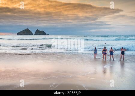 Schwimmerinnen stehen an der Küste am Holywell Beach mit Gull Rocks in der Ferne in Cornwall. Stockfoto