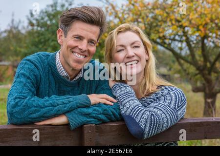 Attraktiv, erfolgreich und glücklich mittleren Alters Mann und Frau zusammen draußen auf einem Zaun in der Landschaft lehnt Stockfoto