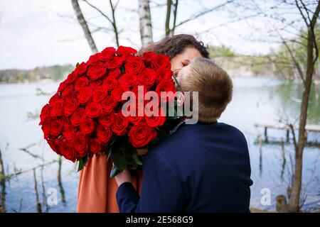 Romantisches Treffen der jungen Leute. Eine junge Frau willigte ein, ihren Mann zu heiraten. Ein Kerl in einem Anzug mit einem Strauß roter Rosen gibt dem Mädchen einen Strauß, und die Stockfoto