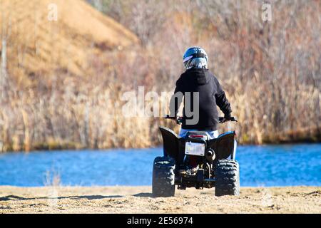 Der Rücken eines Jungen auf einem Quad mit Ein blauer Teich im Hintergrund Stockfoto