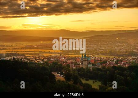 Schöne Luftaufnahme auf Schloss Bojnice und Stadt Bojnice in einem warmen gelben Licht bei Sonnenaufgang, mit interessanten schwarzen Wolken am Himmel Stockfoto