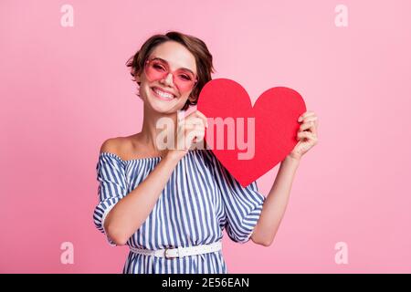 Foto-Porträt von niedlichen Mädchen mit großen roten Herz-Karte mit zwei Händen tragen rosa getönte Gläser isoliert auf pastellrosa Hintergrund. Stockfoto