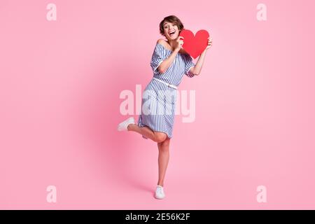Foto-Porträt von schönen Mädchen auf einem Bein mit großen roten Herzen Postkarte isoliert auf pastellrosa farbigen Hintergrund. Stockfoto