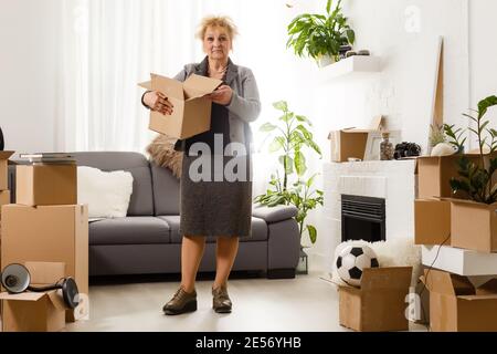 Glücklich aufgeregt reifen Rentner mittleren Alters Frau im modernen stehen Wohnzimmer Interieur allein mit ausgestreckten Armen genießen Freiheit und Wohlfühlgefühl Stockfoto