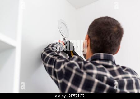 Der Handwerker mit seinem Werkzeug entfernt die Abdeckung von der Lüftungsöffnung in der Wand. Stockfoto