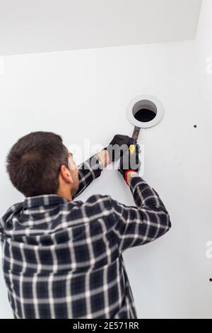 Der Handwerker mit seinem Werkzeug entfernt die Abdeckung von der Lüftungsöffnung in der Wand. Stockfoto