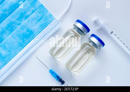 Ein paar Impfstoffflaschen mit sterilen Spritzen und Eine Gesichtsmaske auf weißem Hintergrund Stockfoto