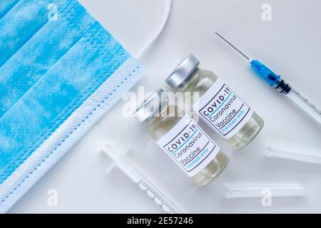 Ein paar Covid-19 Impfstoffflaschen mit sterilen Spritzen Und eine Gesichtsmaske auf weißem Hintergrund Stockfoto