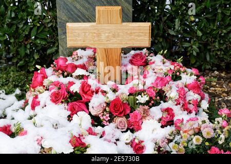 Schneebedeckte Blumendekoration aus Rosen bei einem Grab mit Holzkreuz Stockfoto