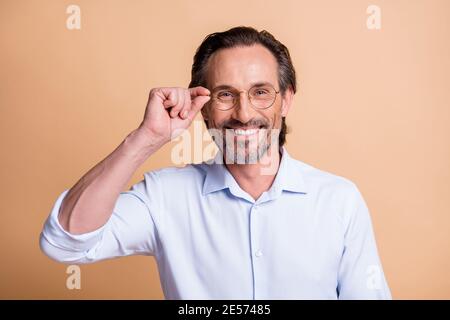 Portrait von schönen fröhlichen Inhalt smart Mann trägt berührende Spezifikationen isoliert über beige Pastellfarbe Hintergrund. Stockfoto