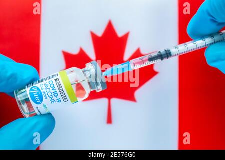 Calgary, Alberta. Kanada. Januar 20 2021. Ein Gesundheitshelfer mit einem Pfizer-Impfstoff und einer Spritze mit einer kanadischen Flagge auf dem Hintergrund Stockfoto