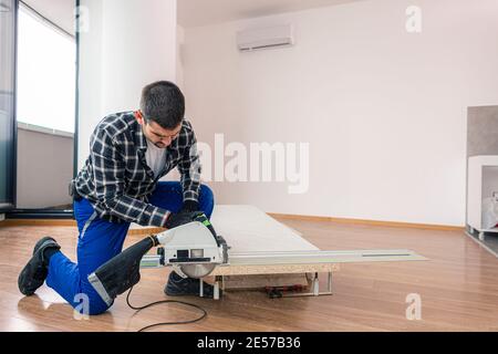 Ein Zimmermann schneidet eine Holzdiele der Arbeitsfläche auf dem Boden des Raumes. Er führt seine Arbeitsaufgabe auf einer Holzkiste aus, die ihm als Werk diente Stockfoto