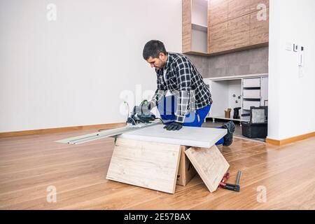 Ein Zimmermann schneidet eine Holzdiele der Arbeitsfläche auf dem Boden des Raumes. Er führt seine Arbeitsaufgabe auf einer Holzkiste aus, die ihm als Werk diente Stockfoto