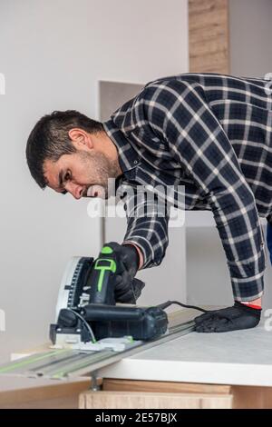 Ein Zimmermann schneidet eine Holzdiele der Arbeitsfläche auf dem Boden des Raumes. Er führt seine Arbeitsaufgabe auf einer Holzkiste aus, die ihm als Werk diente Stockfoto