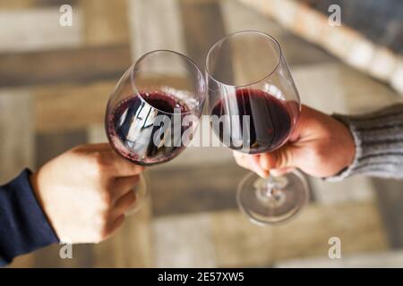 Nahaufnahme der Hände von zwei unbekannten kaukasischen Männern Gläser mit Rotwein-Toasting - Mann jubelt feiern während Trinken zu Hause oder im Restaurant Stockfoto