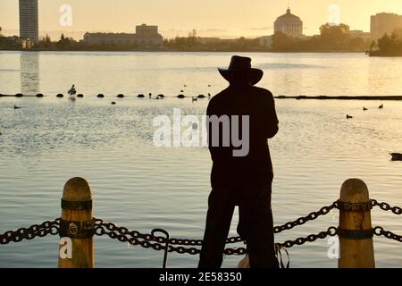 Silhouette eines Mannes, der bei Sonnenuntergang vor dem Lake Merritt vor Kettengliedern steht, Oakland, Kalifornien, USA Stockfoto