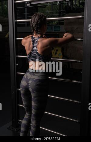 Das Mädchen lehnt sich im Dunkeln an die schwedische Treppe. Metallic in einer schönen Form eines Fitness-Studio eines Fitness-Club mit einem Rücken in einem Trainingsanzug für Adverti Stockfoto